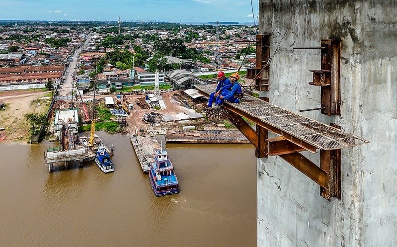 Vista do alto mostra trabalhador olhando obra à beira do rio