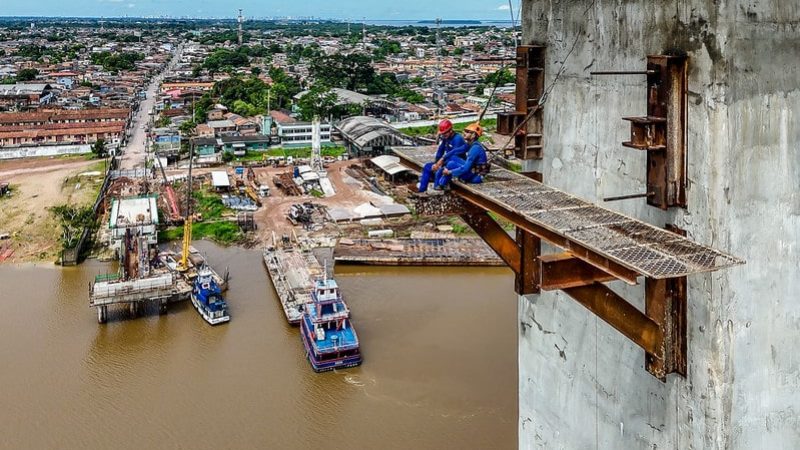 Vista do alto mostra trabalhador olhando obra à beira do rio